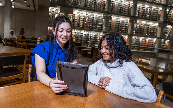 Two women using a tablet in a library.
